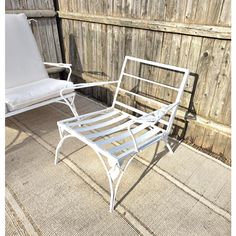 a white metal chair sitting on top of a rug next to a wooden fence and wall