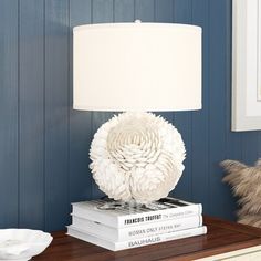 a lamp sitting on top of two books in front of a blue wall and white flowers