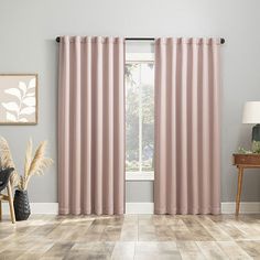 a living room with pink curtains and wood floors in front of a large window that has a plant next to it