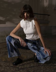 a woman sitting on the ground with her legs crossed, wearing jeans and a white top