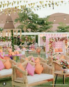 an outdoor event with pink and orange pillows on wooden chairs, white cushions, and hanging lights