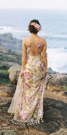 a woman standing on top of a rocky cliff next to the ocean wearing a floral dress