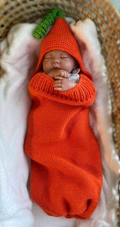 a newborn baby wrapped in an orange knitted blanket with a green leaf on it's head