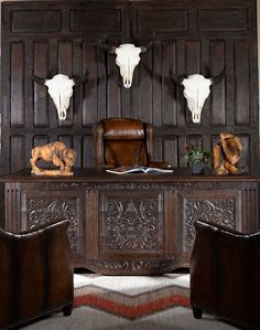 an old wooden desk with two steer heads on the wall and leather chairs in front of it