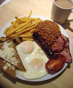 a breakfast plate with eggs, bacon, beans and toast on it next to a cup of coffee