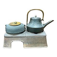 a tea pot and kettle sitting on top of a metal stand with a white background