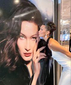 a woman standing next to a large poster with her hand on her face and another woman touching her cheek