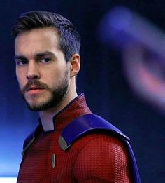 a close up of a person wearing a red and blue suit with a beard in front of a dark background