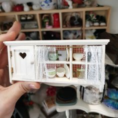 someone is holding up a miniature dollhouse with cups and saucers in the window