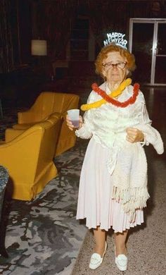 an older woman wearing a tiara and holding a cup in her hand while standing next to a couch