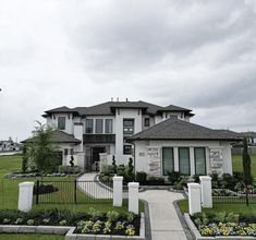 a large house with lots of plants and flowers in front of it on a cloudy day