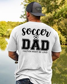 a man wearing a soccer dad t - shirt and hat standing next to a body of water