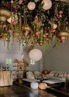 a living room filled with lots of plants and hanging lights above the couches in front of them