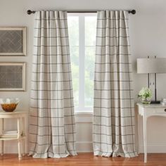 a living room with white walls and wooden floors, two windows covered in plaid curtains