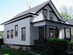 a white house with black trim on the front and side windows, sitting next to a green lawn