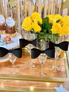 a table topped with wine glasses filled with yellow flowers and cupcakes on top of it