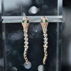 A ladies pair of 14 karat yellow gold snake dangle earrings set with 54 round brilliant cut diamonds having a total weight of .29 carats and 4 round emerald eyes having a total weight of .03 carats. Luxury White Gold Earrings With Diamond Eyes, Gold Dangle Earrings With Diamond Eyes, Gold Drop Earrings With Diamond Eyes, Yellow Gold Earrings With Diamond Eyes For Anniversary, Handmade Gold Cubic Zirconia Earrings, Yellow Gold Diamond Eyes Earrings For Anniversary, Anniversary Yellow Gold Earrings With Diamond Eyes, Handmade Gold Snake-shaped Earrings, Luxury Gold Earrings With Diamond Eyes