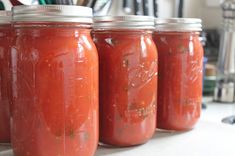 four jars filled with tomato sauce sitting on top of a counter next to utensils