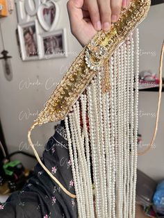 a person holding up a gold and white beaded purse with chains hanging from it