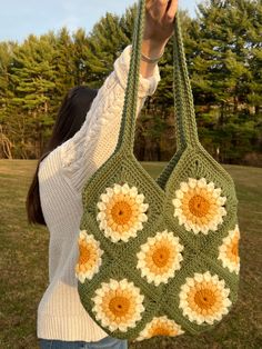 a woman holding up a crocheted bag with sunflowers on the front