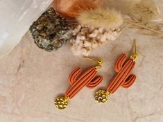 an orange pair of earrings sitting on top of a table next to some rocks and feathers