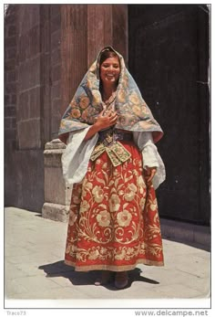 a woman dressed in an elaborately designed dress and head scarf is standing on the sidewalk