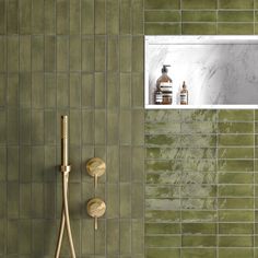 a green tiled bathroom with gold fixtures and soap dispensers on the wall