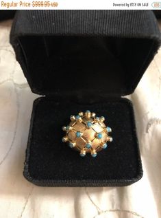 an antique ring with turquoise stones sits in a black box on a white cloth covered surface