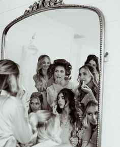 a woman standing in front of a mirror brushing her teeth with other women looking on