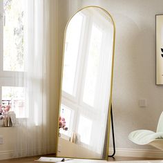 a large mirror sitting on top of a wooden floor next to a white chair and window