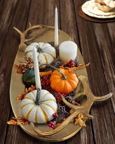 a plate with pumpkins, candles and other autumn decorations on it sitting on a wooden table