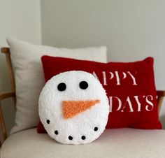 a snowman pillow sitting on top of a white couch next to a red pillow