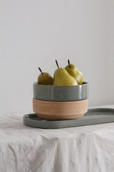 a bowl filled with green apples on top of a white cloth covered table next to a metal tray