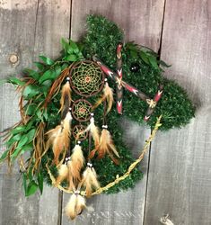 a wreath made out of moss with feathers and beads on it, sitting on a wooden surface