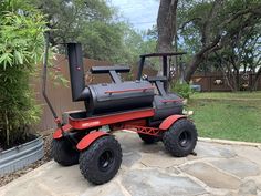 a red and black tractor sitting on top of a stone patio next to a tree