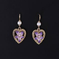 Antique Violet Heart Earrings: Adorn yourself with the charming elegance of these earrings featuring purple enamel violets nestled within hearts of pearls, all set in gleaming 14k gold. Transformed from an antique pin dating back to 1910-1920, they now boast gold ear wires and pearl surmounts, exuding timeless sophistication and vintage allure. Each earring measures 1 inch from the top of the ear wire to bottom by 0.4 inches wide and are in great condition. Upon purchase, your earrings will arrive elegantly packaged, ready for gifting or as a special treat for yourself.  We carefully wrap each piece to ensure a delightful unboxing experience. We also offer free and flexible layaway plans, so take advantage of this option to make owning your dream piece even more achievable. + Trademark Ant Elegant Heart-shaped Enamel Earrings, Elegant Enamel Heart Earrings For Gift, Elegant Heart Enamel Earrings For Gift, Violet Heart, Antique Pins, Bespoke Rings, The Ear, Ear Wire, Heart Earrings