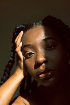 a woman with black makeup and braids holding her hand up to her face while looking at the camera