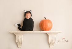 a baby in a cat costume sitting on top of a shelf next to a pumpkin