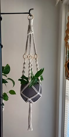 a macrame plant hanging from a hook on a wall next to a potted plant