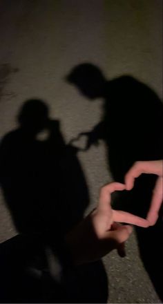 the shadow of a person holding a cell phone in their hand and making a heart shape