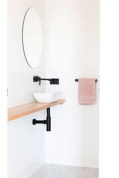 a white sink sitting under a bathroom mirror next to a shelf with a pink towel on it