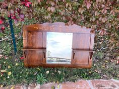 a mirror sitting on top of a wooden shelf next to a tree filled with leaves