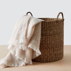 a woven basket with a white towel in it sitting on a table next to a brown wicker basket