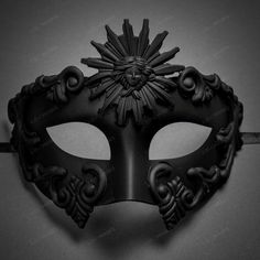 a black mask with an ornate design on the front and side, sitting against a gray background