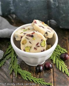 some cookies are in a white bowl on a wooden table next to berries and leaves