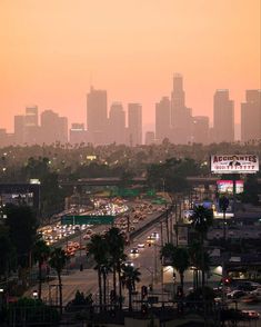 the city skyline is lit up at dusk with traffic driving down it and palm trees in the foreground