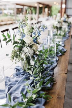 a long table is set with blue and white flowers, greenery, and candles