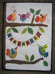 a quilted wall hanging with colorful birds on it's branches and bunting