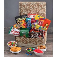 a box filled with candy and snacks on top of a wooden table next to bowls