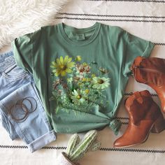 Imagine strolling through a picturesque meadow, surrounded by a kaleidoscope of colors and the delicate fragrance of wildflowers in the air. Our Vintage Wildflowers t-shirt allows you to carry that serene and timeless beauty with you wherever you go. Perfect for nature enthusiasts, garden lovers, or those seeking a touch of vintage charm in their wardrobe, this shirt is a versatile addition to any outfit. Whether you pair it with your favorite jeans or dress it up with a flowy skirt, this t-shir Botanical Green Tops With Plant Print, Green Tops With Plant Print For Spring, Green Cottagecore Top For Spring, Green Cottagecore Tops For Spring, Spring Graphic Tee Shirt In Green, Green Cotton Shirt With Floral Print, Green Botanical Print Tops, Green Cotton Shirt With Plant Print, Green Cotton Top With Sunflower Print